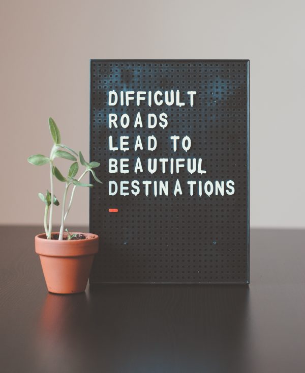 A letter board on a desk reading “Difficult roads lead to beautiful destinations” next to a seedling